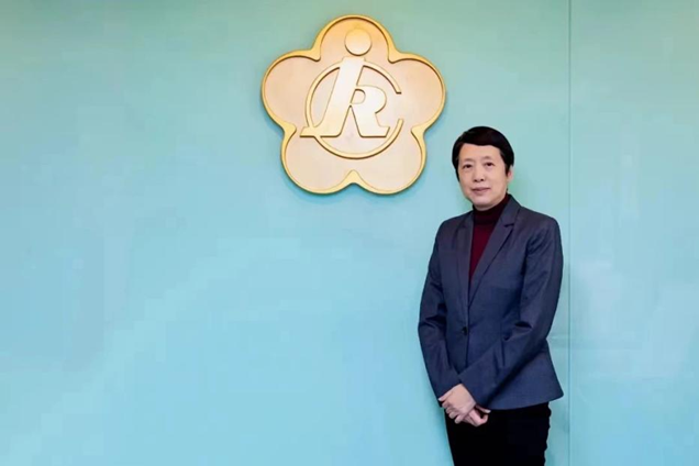 圖為龍墨在中國殘疾人福利基金會會徽前留影